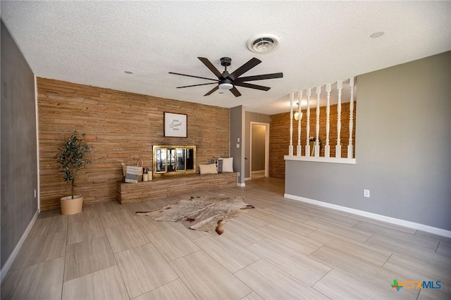 unfurnished living room with visible vents, a fireplace, wooden walls, and a textured ceiling