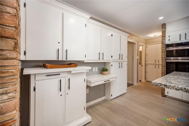 kitchen with light countertops, stainless steel double oven, white cabinets, and ornamental molding