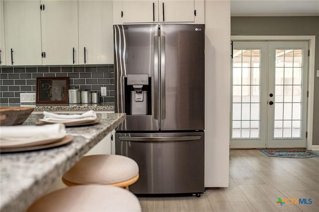 kitchen featuring french doors, stainless steel refrigerator with ice dispenser, backsplash, and white cabinetry