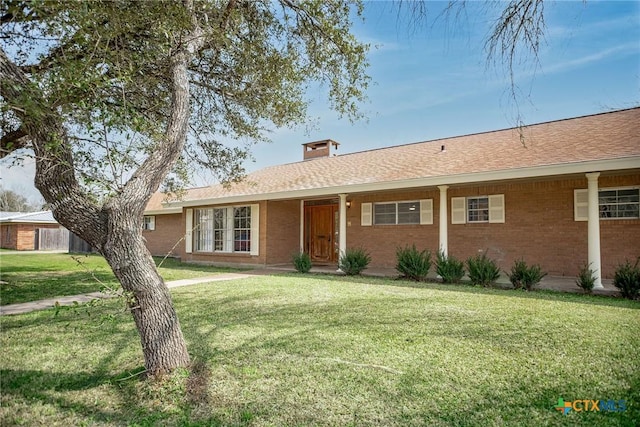 ranch-style house featuring roof with shingles, brick siding, a chimney, and a front yard