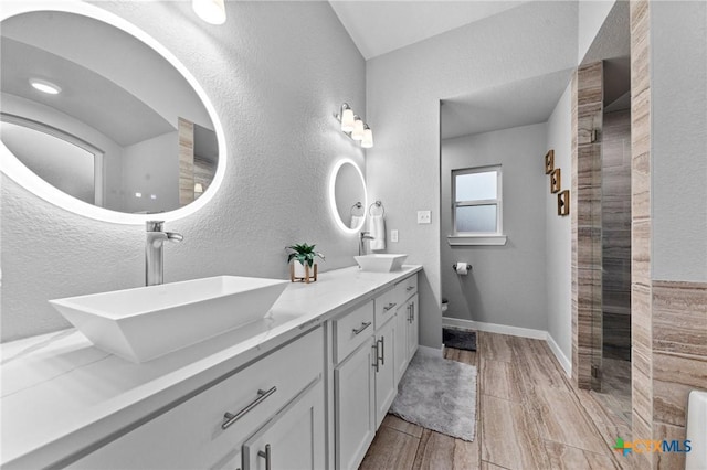 full bath with double vanity, baseboards, a sink, and tiled shower