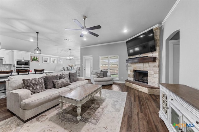 living room featuring dark wood finished floors, a ceiling fan, crown molding, and a stone fireplace