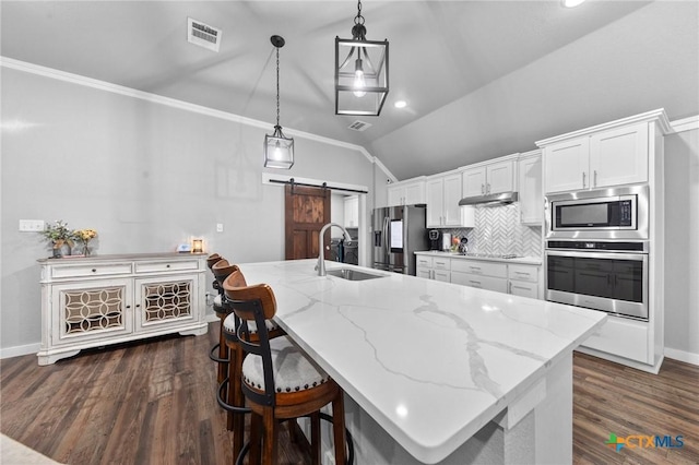 kitchen featuring hanging light fixtures, a barn door, appliances with stainless steel finishes, white cabinets, and a sink