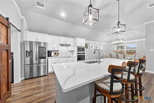 kitchen featuring a barn door, white cabinets, stainless steel appliances, pendant lighting, and a sink