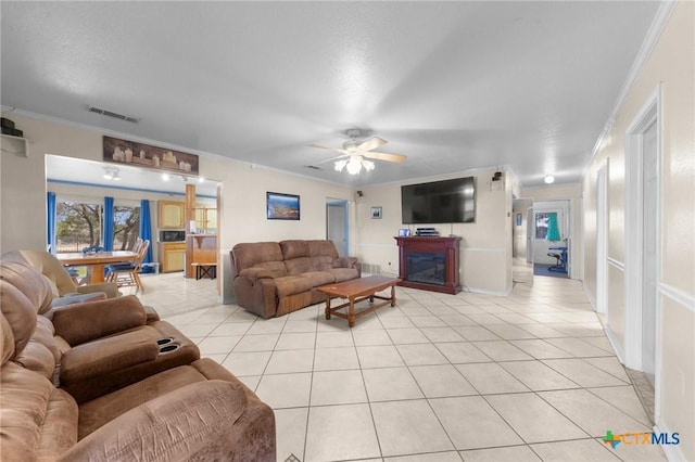 living room with a glass covered fireplace, visible vents, a ceiling fan, crown molding, and light tile patterned floors