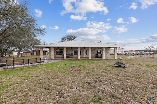 rear view of house with a patio area, a lawn, a fire pit, fence, and metal roof