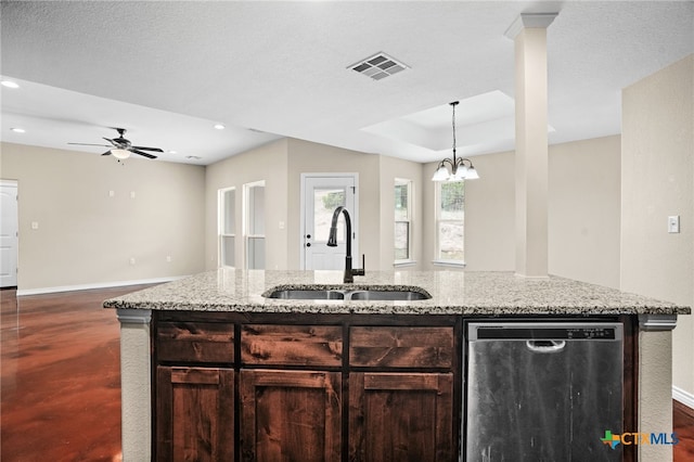 kitchen with sink, light stone counters, a center island with sink, stainless steel dishwasher, and a tray ceiling