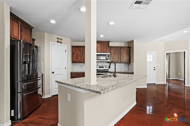 kitchen with appliances with stainless steel finishes, sink, backsplash, a kitchen island with sink, and light stone countertops