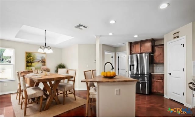 kitchen with a breakfast bar, pendant lighting, a kitchen island with sink, a notable chandelier, and stainless steel refrigerator with ice dispenser