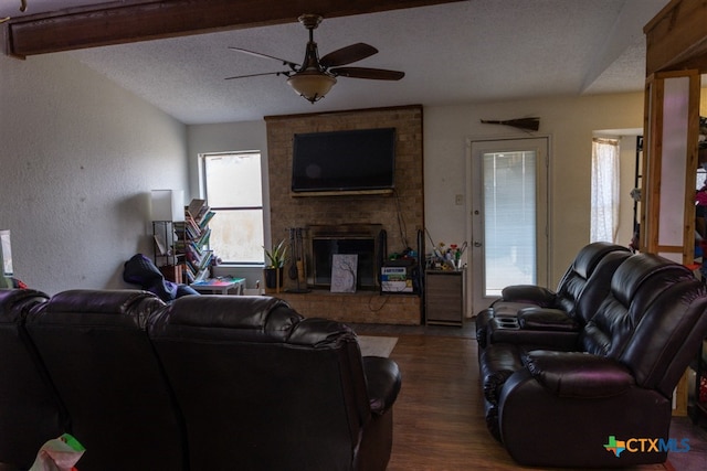 living room featuring a textured ceiling, a textured wall, dark wood-type flooring, a fireplace, and a ceiling fan