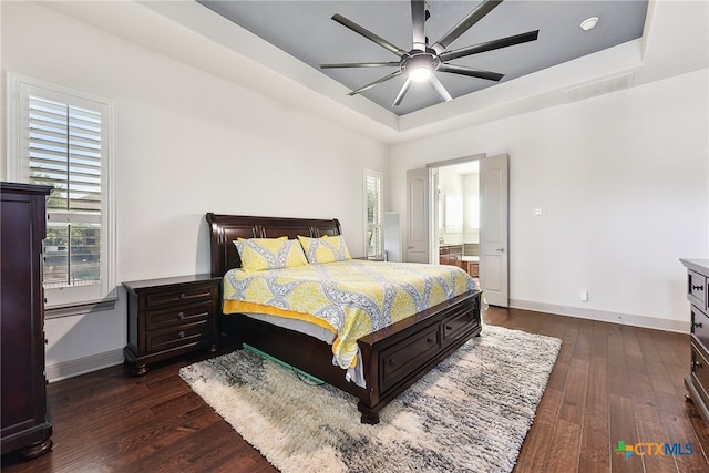 bedroom featuring ceiling fan, dark hardwood / wood-style flooring, a tray ceiling, and ensuite bath