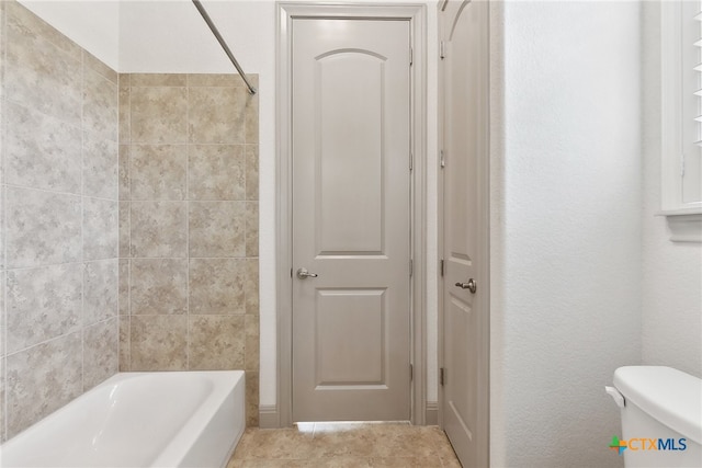 bathroom featuring tile patterned flooring, toilet, and tiled shower / bath