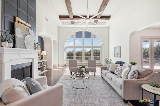 living room featuring beam ceiling, hardwood / wood-style flooring, ceiling fan, and a high ceiling