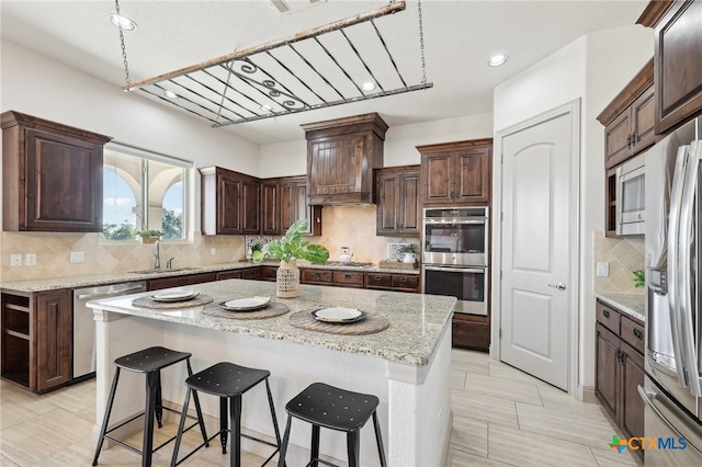 kitchen featuring light stone countertops, decorative backsplash, stainless steel appliances, sink, and a kitchen island