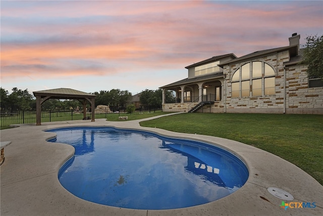 pool at dusk featuring a gazebo, a patio area, and a lawn