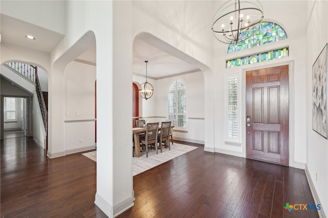 foyer entrance featuring ornamental molding, dark wood-type flooring, and an inviting chandelier