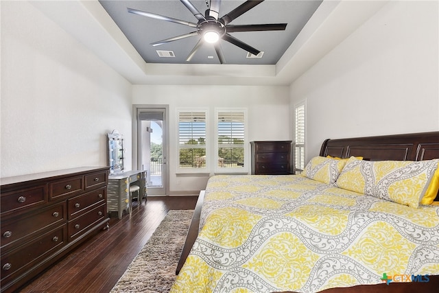 bedroom featuring ceiling fan, dark hardwood / wood-style flooring, access to outside, and a tray ceiling