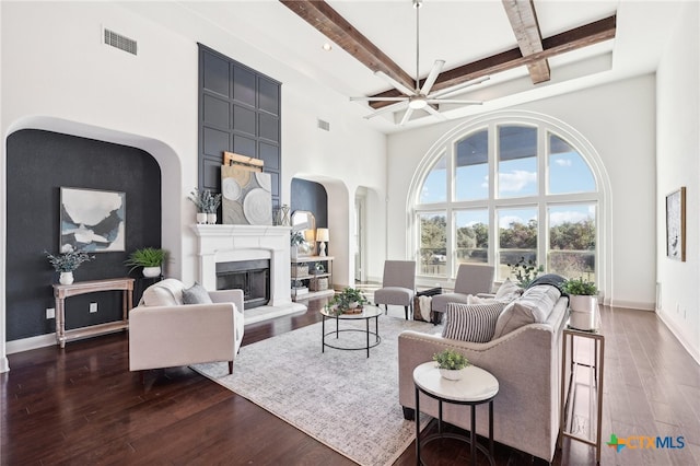 living room with beamed ceiling, ceiling fan, dark wood-type flooring, and a high ceiling