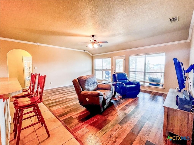 living room featuring ceiling fan, ornamental molding, wood-type flooring, and a textured ceiling