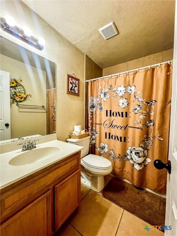 bathroom with toilet, tile patterned flooring, vanity, and a textured ceiling