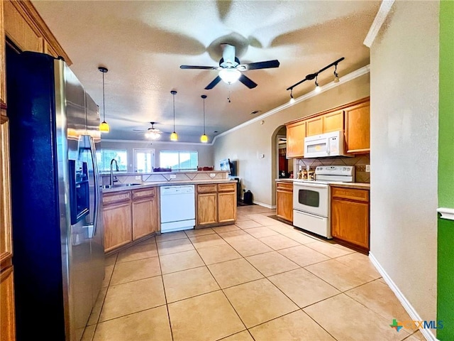 kitchen featuring kitchen peninsula, hanging light fixtures, sink, white appliances, and crown molding