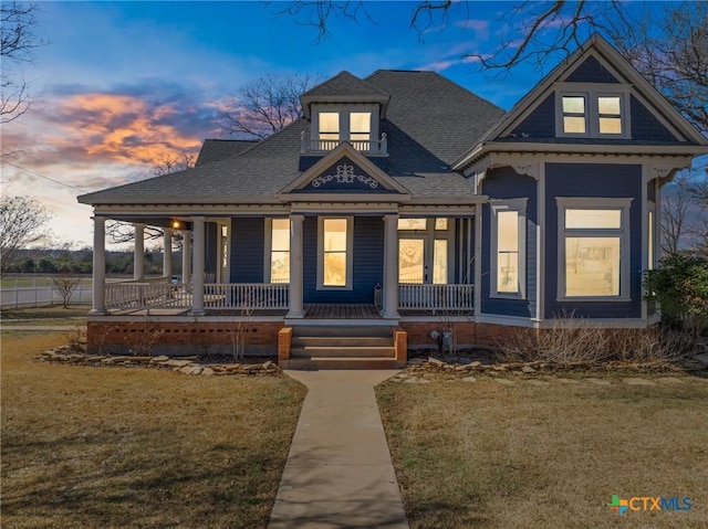 view of front of property featuring a porch, a front lawn, and a shingled roof