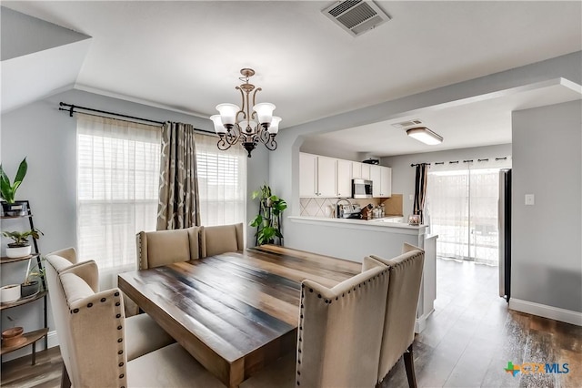 dining room with dark hardwood / wood-style flooring, vaulted ceiling, and an inviting chandelier