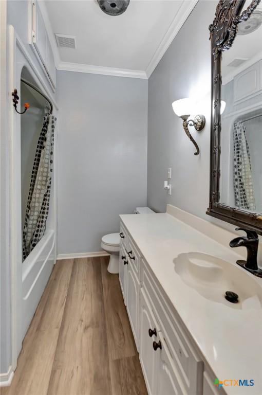 full bathroom with vanity, toilet, shower / bathtub combination with curtain, ornamental molding, and wood-type flooring