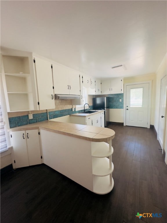 kitchen with tasteful backsplash, stainless steel fridge, white cabinetry, dark wood-type flooring, and kitchen peninsula