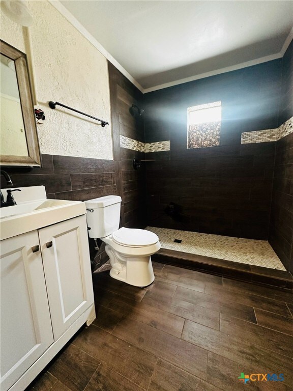 bathroom with ornamental molding, wood-type flooring, vanity, toilet, and tile walls