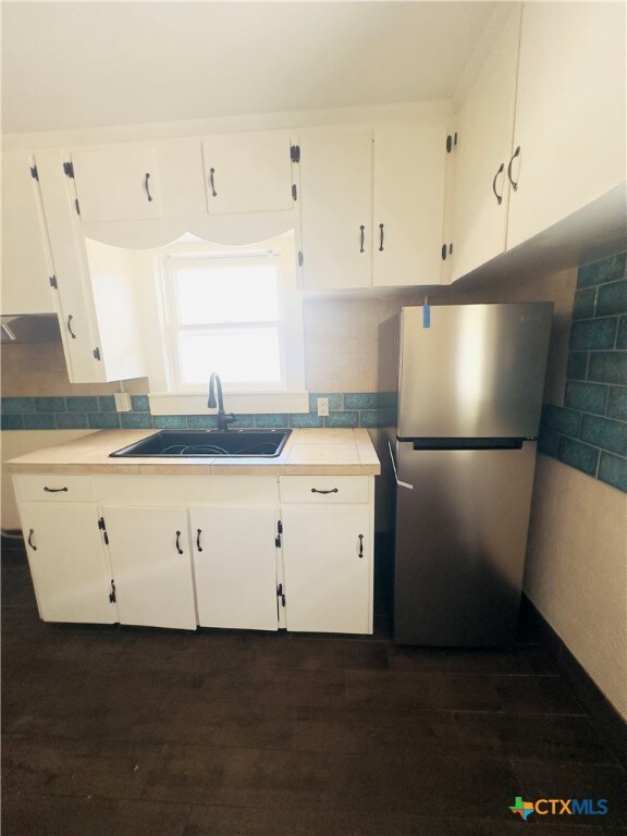 kitchen with white cabinets, sink, backsplash, and stainless steel refrigerator