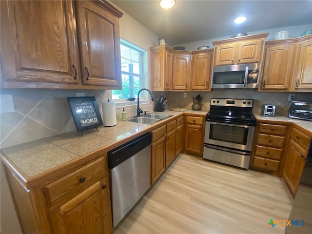kitchen featuring light wood-type flooring, brown cabinets, tasteful backsplash, a sink, and appliances with stainless steel finishes