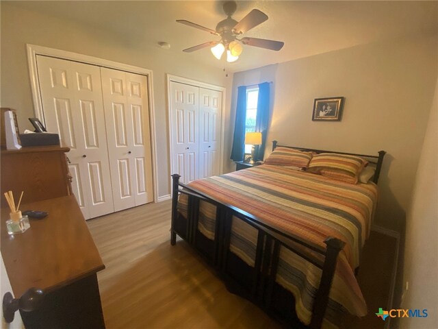 bedroom with baseboards, ceiling fan, multiple closets, and wood finished floors