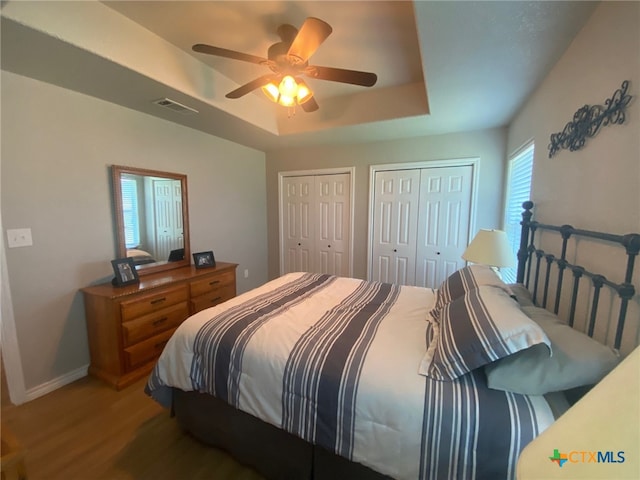 bedroom featuring light wood-style floors, multiple closets, baseboards, a tray ceiling, and visible vents