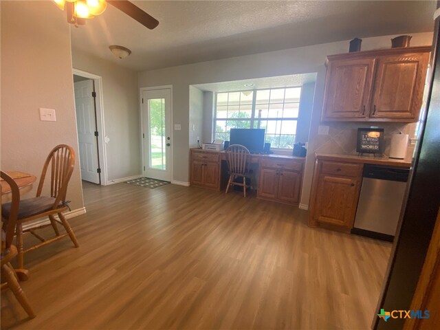 interior space featuring brown cabinets, light wood finished floors, a ceiling fan, baseboards, and stainless steel dishwasher