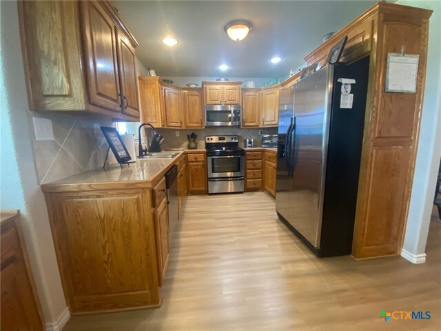 kitchen with appliances with stainless steel finishes, a sink, light countertops, light wood-style flooring, and decorative backsplash