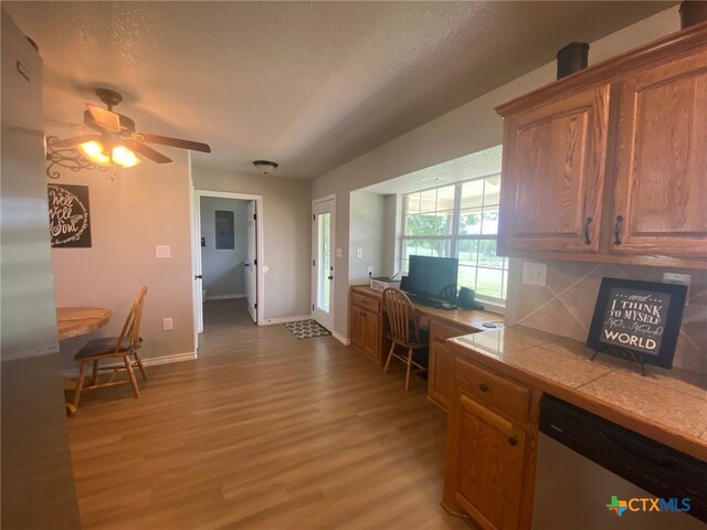 kitchen with ceiling fan, dishwasher, light wood-style flooring, tile countertops, and baseboards