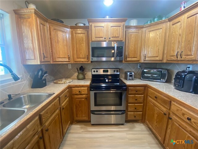 kitchen with brown cabinetry, a sink, appliances with stainless steel finishes, and a toaster