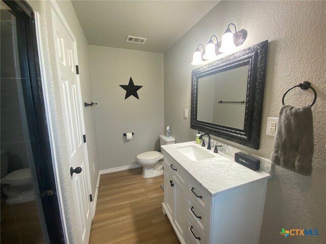 bathroom featuring toilet, visible vents, wood finished floors, and vanity