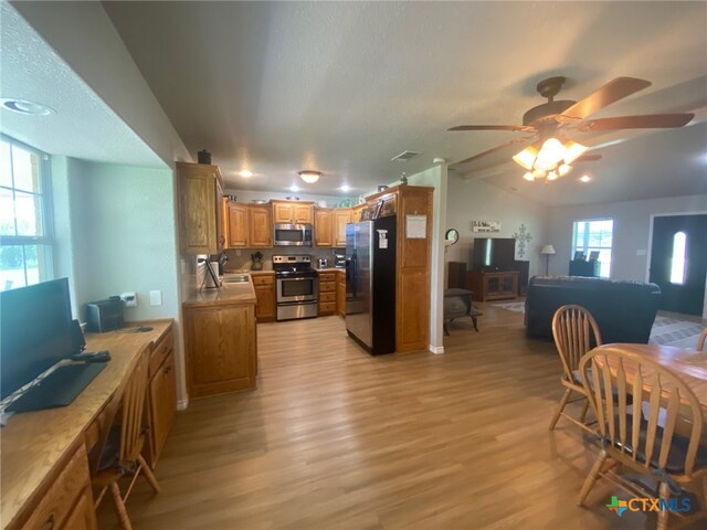 kitchen featuring ceiling fan, brown cabinetry, open floor plan, stainless steel appliances, and light wood-style flooring