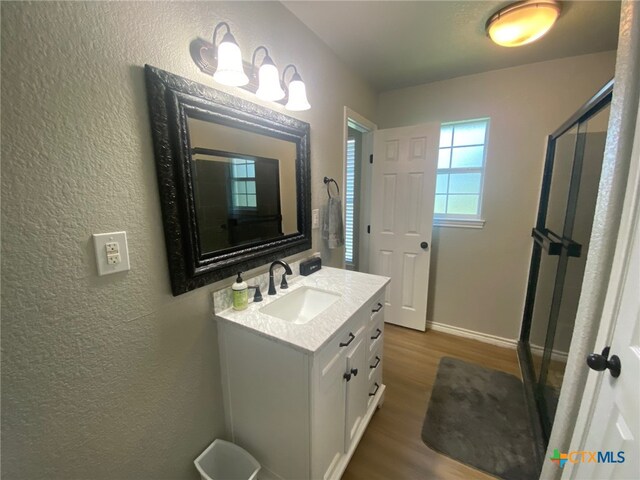 full bathroom with a shower stall, wood finished floors, vanity, baseboards, and a textured wall