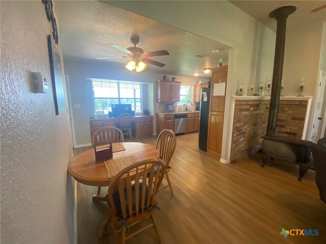 dining area featuring a wood stove, a textured ceiling, a ceiling fan, light wood-type flooring, and visible vents