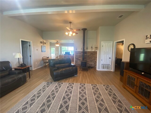 living room with ceiling fan, a wood stove, baseboards, wood finished floors, and visible vents