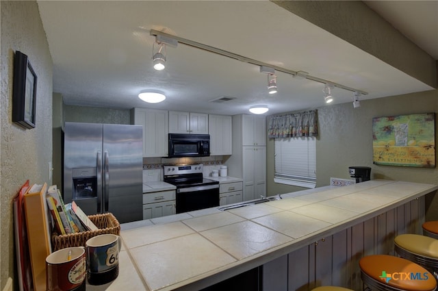 kitchen with appliances with stainless steel finishes, a kitchen breakfast bar, sink, kitchen peninsula, and tile countertops