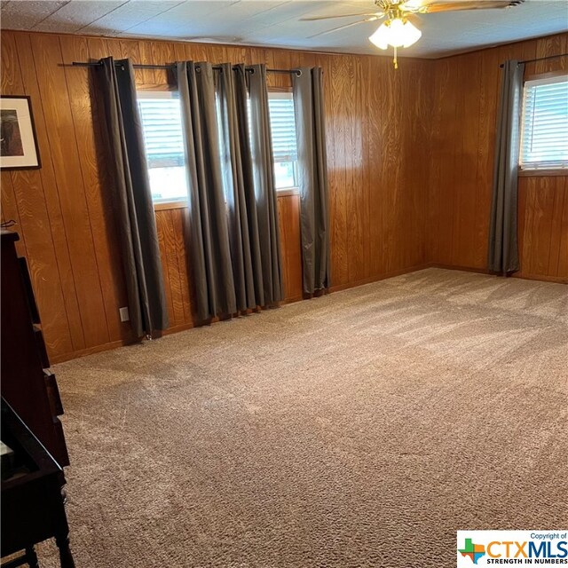 carpeted empty room featuring wood walls, ceiling fan, and plenty of natural light