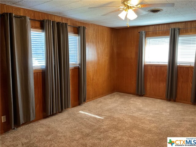 carpeted empty room with wood walls and ceiling fan