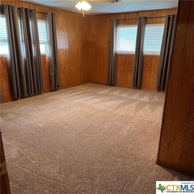 unfurnished room with plenty of natural light, light carpet, ceiling fan, and wooden walls