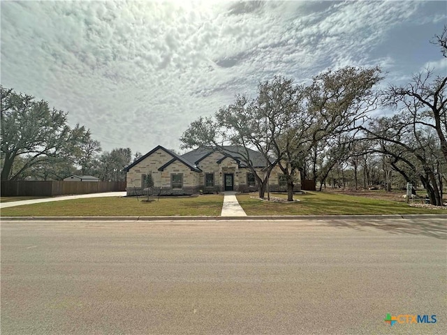 french provincial home with a front yard, stone siding, and fence