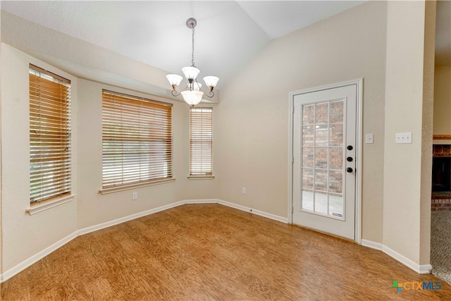 unfurnished dining area with a fireplace, light hardwood / wood-style flooring, vaulted ceiling, and a notable chandelier