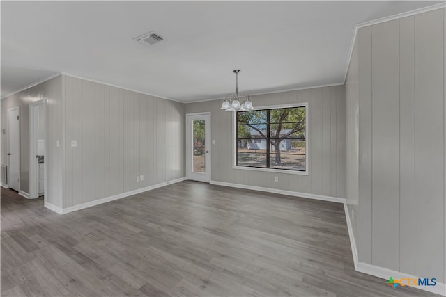 unfurnished dining area featuring wood walls, a notable chandelier, light hardwood / wood-style floors, and crown molding